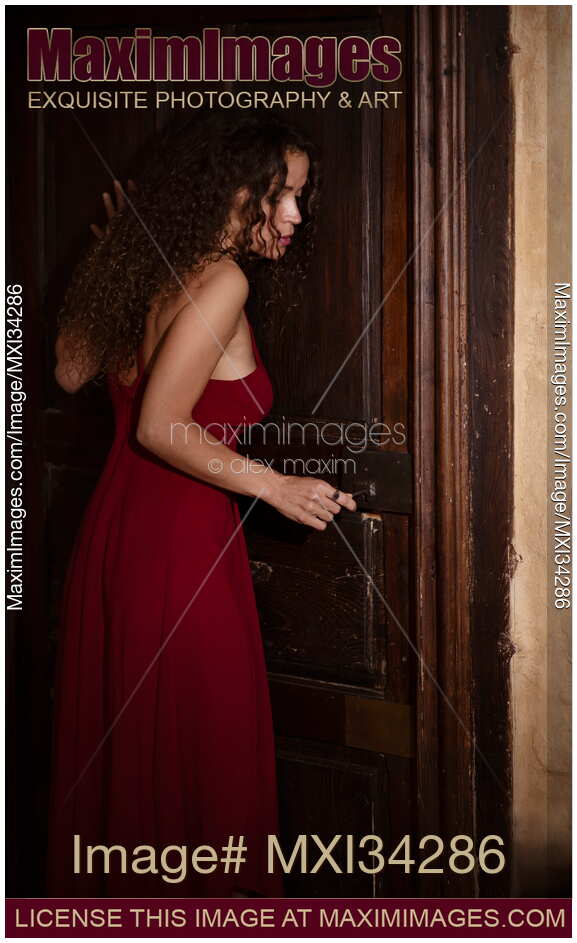 Woman in red dress cautiously listening to the door while opening the lock