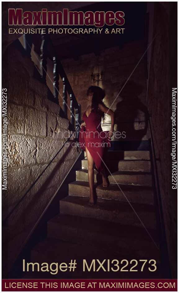 Woman in red dress running away down the staircase of an old house