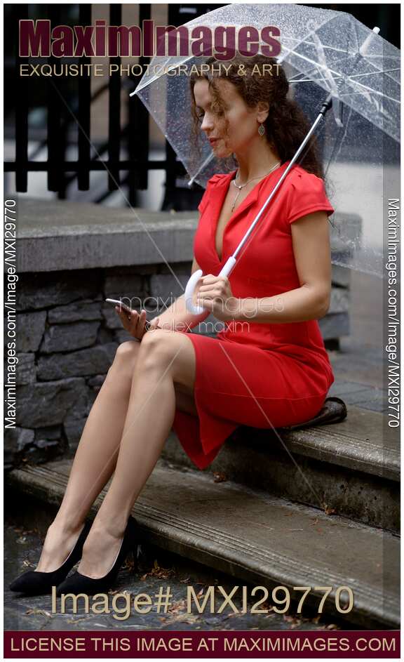 Woman in red dress sitting on the street under umbrella with cellphone