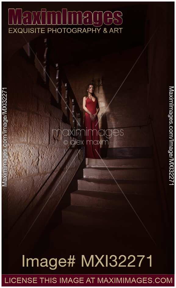 Woman in red dress standing like a ghost on dark house staircase looking down with a stern expression