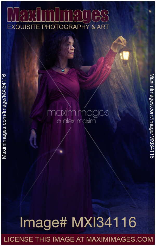 Woman in red dress walking with a lit lantern in her hand in a dark forest