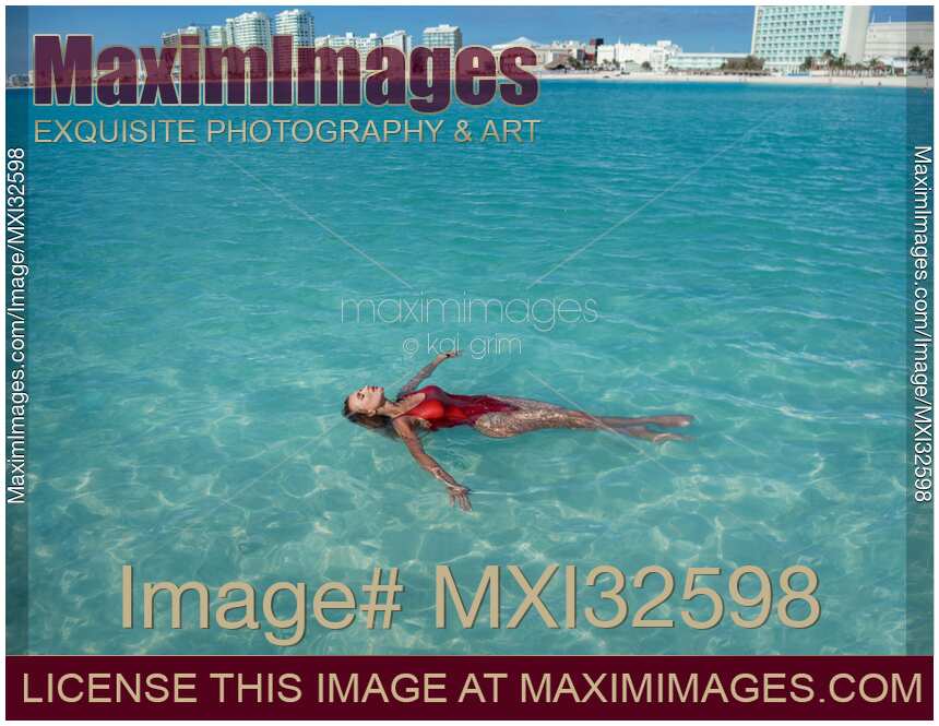 Woman in red swimsuit lying in clear blue water of Caribbean Sea with Cancun city skyline in the background