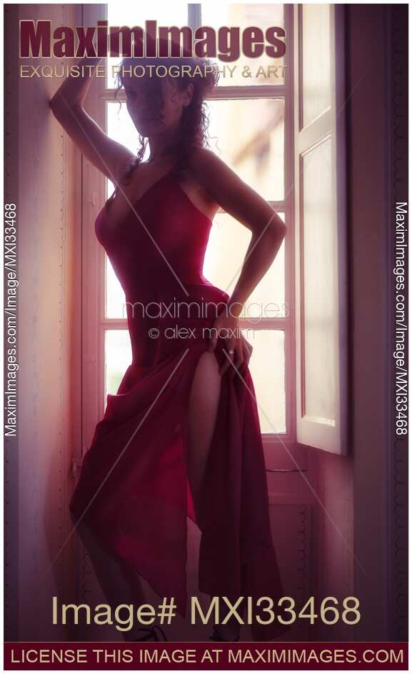 Woman in sexy elegant red dress standing by a bright French window in a seductive pose