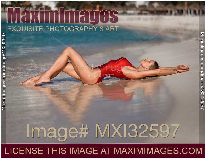Woman in sexy red swimsuit lying on a sandy shore of Caribbean Sea beach in Cancun