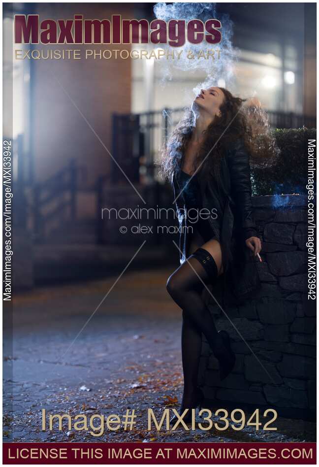 Woman in sexy stylish black clothes smoking a cigarette on night city street with an expression of abandon