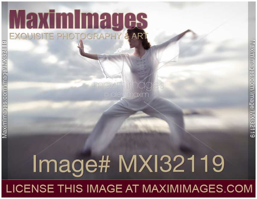 Woman in sheer white clothes practicing Tai Chi on the ocean shore in sunrise