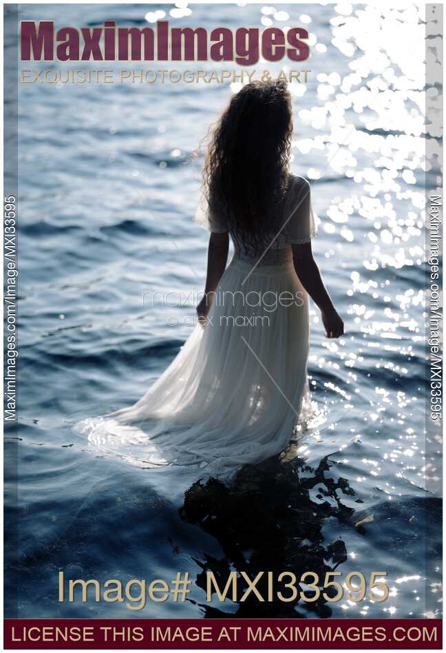 Woman in sheer white dress standing in the water in sunshine