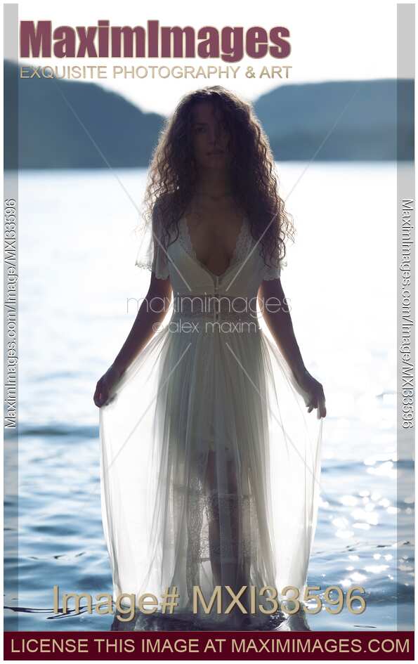 Woman in sheer white lace dress walking out of sea water in bright sunlight like a beautiful Greek Goddess