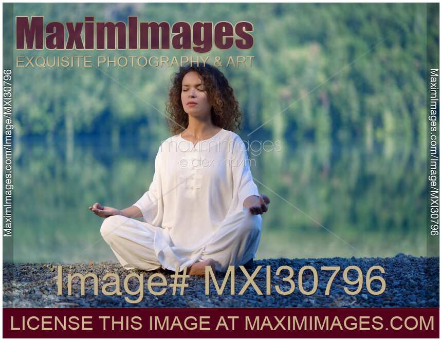 Woman in white clothes meditating in the morning sunrise by the lake