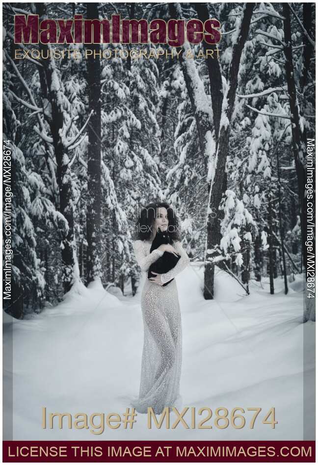 Woman in white dress walking in snow with a black cat in her hands
