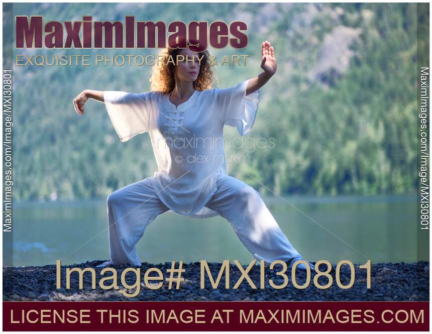 Woman in white outfit practicing Tai Chi stance by the lake in the nature