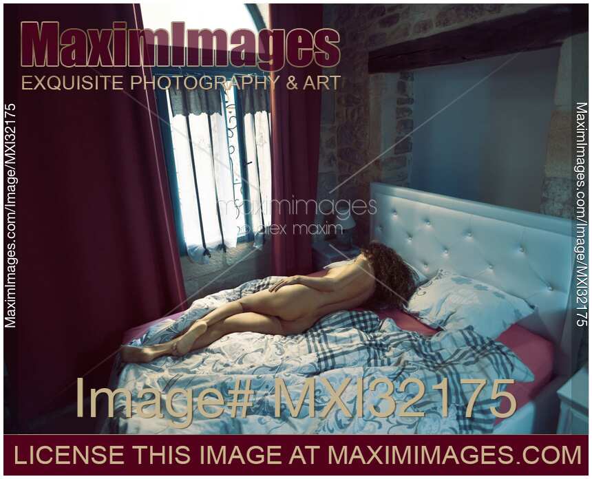 Woman lying asleep naked on a bed in morning light from a window