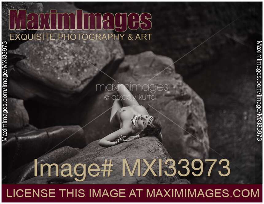 Woman lying naked on the rocks in nature scenery. Black and white art nude photograph.