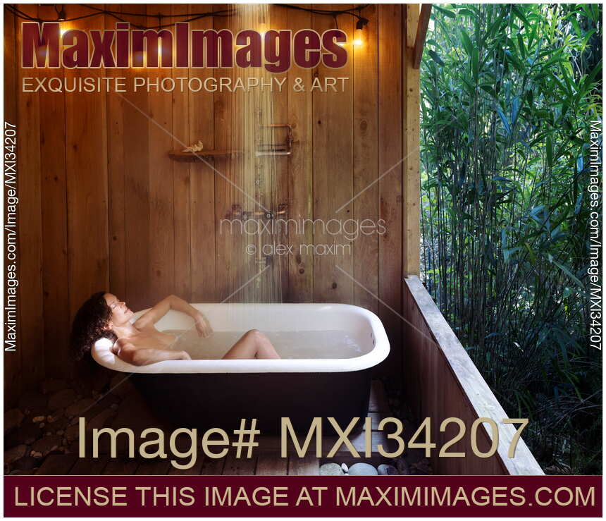 Woman lying naked relaxed in open-air bath tub in a rustic countryside cabin
