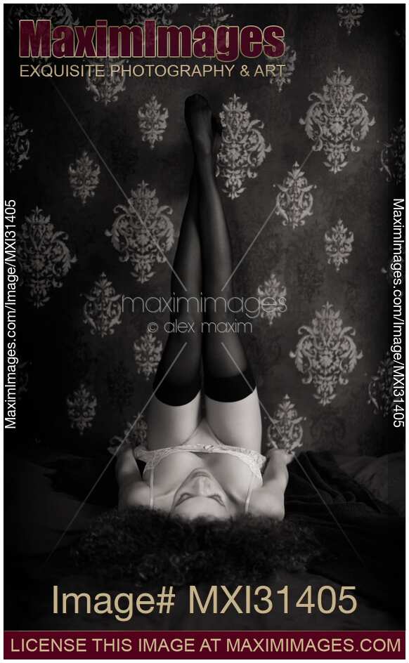 Woman lying on a bed in lingerie with sexy long legs in stockings up against the wall Black and white