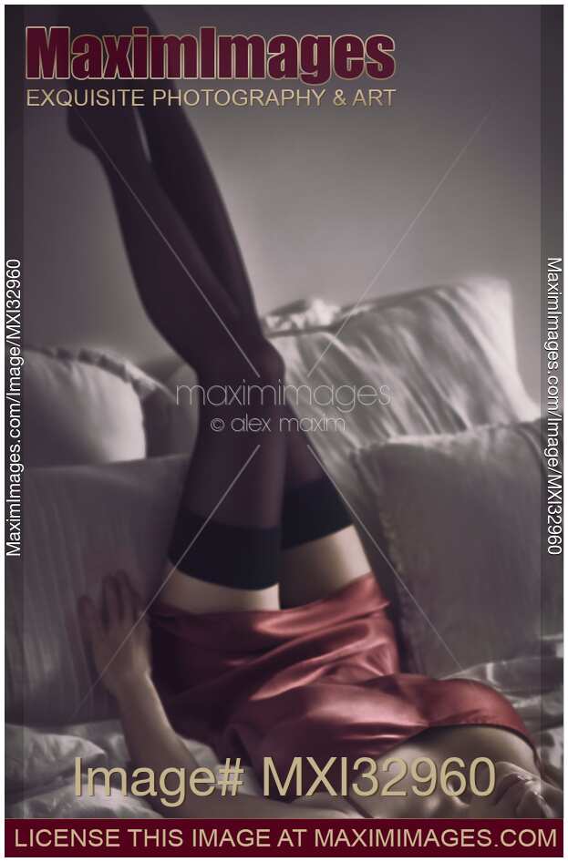 Woman lying on bed in sexy silk red nightgown with her long legs in stockings up against the wall