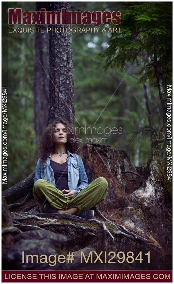 Woman meditating in forest sitting in meditation pose leaning against tree trunk in nature