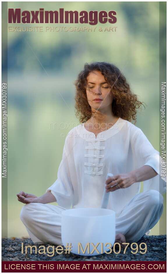 Woman meditating with a quartz crystal singing bowl in the morning by the lake in the nature