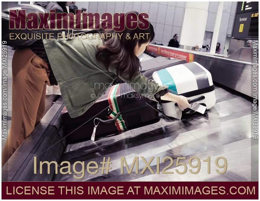 Woman picking up suitcase from airport baggage claim conveyor