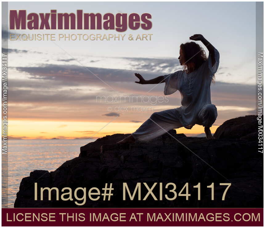 Woman practicing Tai Chi at rocky sea shore during sunset