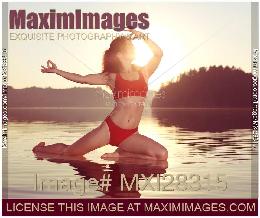 Woman practicing yoga on the water doing Pigeon pose in morning sunlight