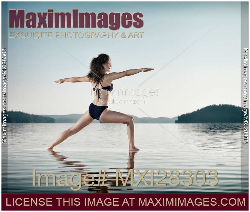 Woman practicing yoga on the water doing Warrior pose over blue sky