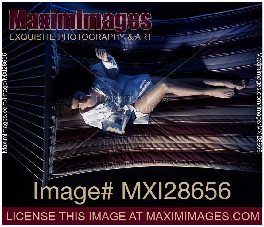 Woman reading a book in a hammock at night in dim light