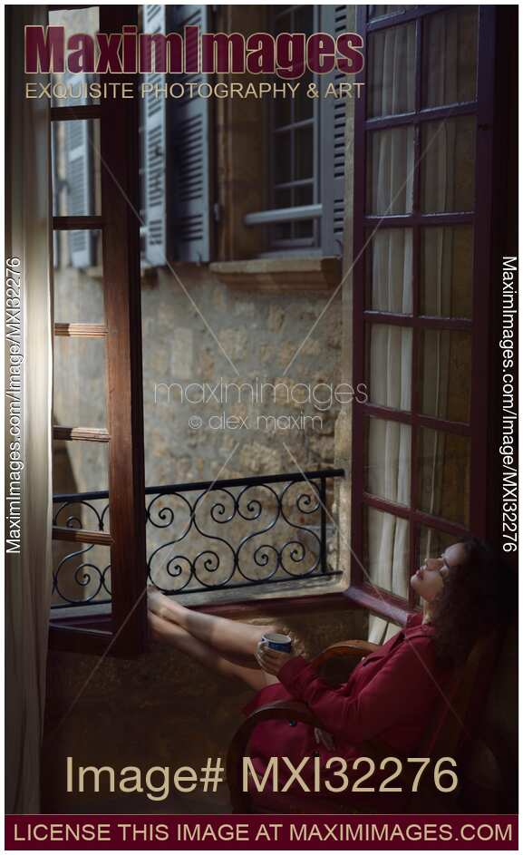 Woman resting in a chair by an open windows in France holding a cup of coffee in her hand