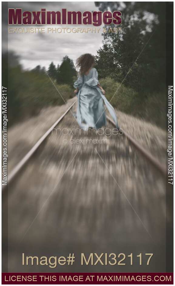 Woman running away along railroad tracks in a long dress flying in the wind