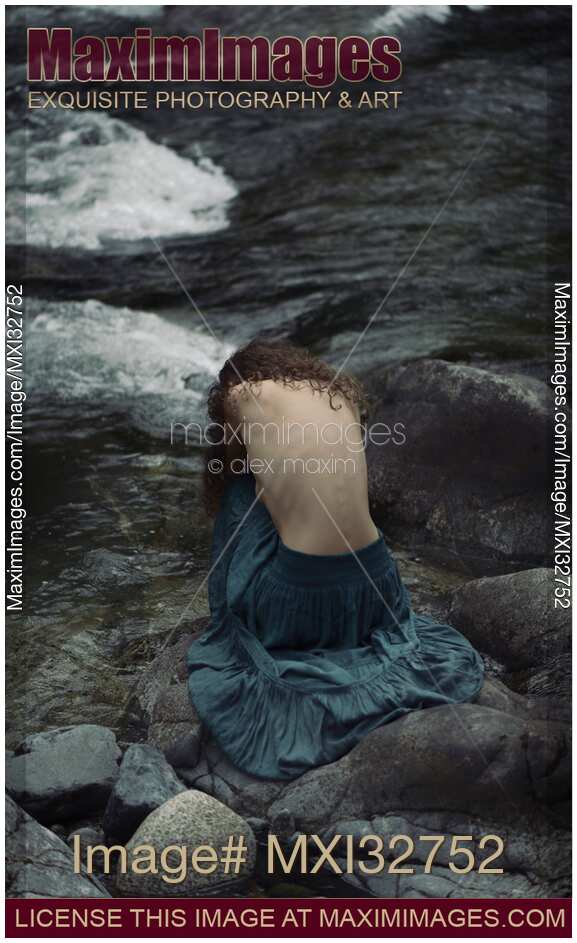 Woman sitting curled up by the river with her bare back exposed Dramatic fine art photograph