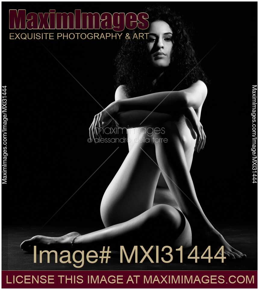 Woman sitting naked with arms and legs crossed in front of her nude body