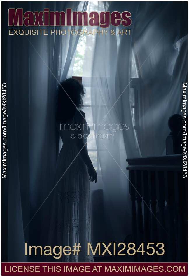 Woman standing at window in dark room in dim sunlight