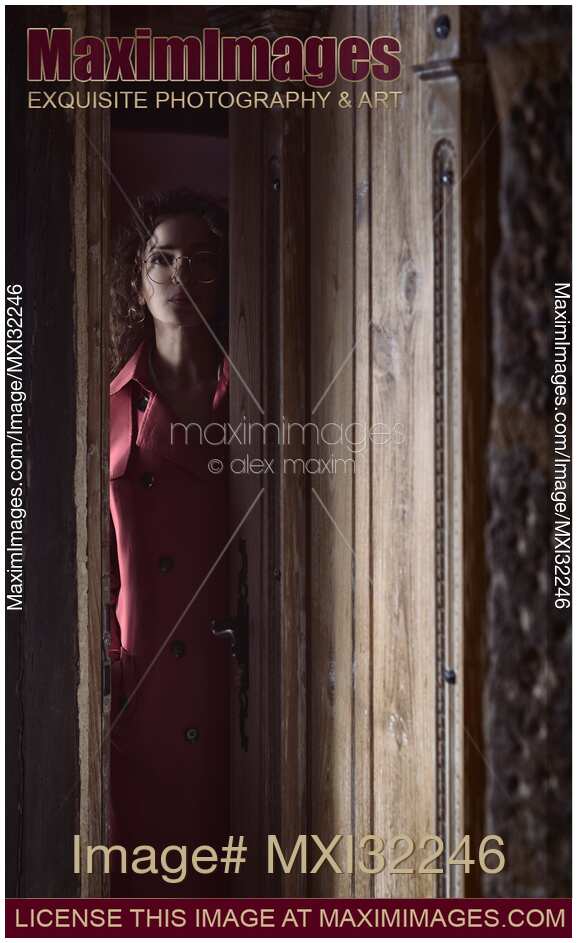 Woman standing behind a slightly opened entrance door of a house looking out at a night visitor