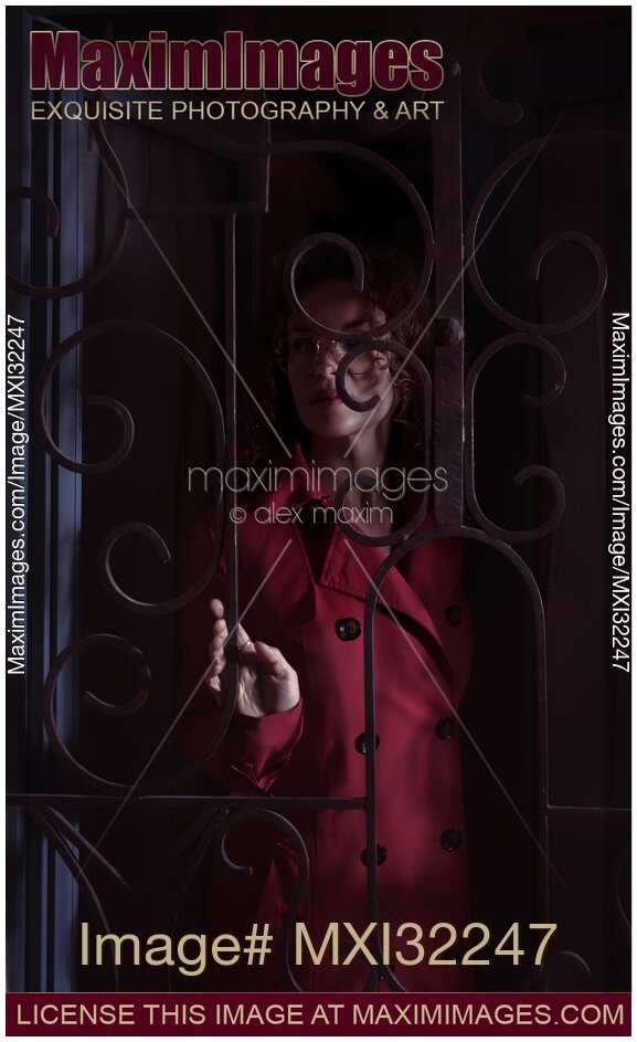 Woman standing behind locked grates touching the metal bars in a dark room