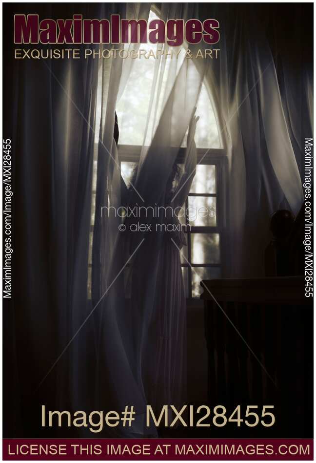 Woman standing behind the curtains at window in dark room