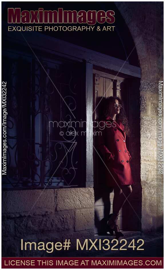 Woman standing on the street at night leaning against a locked door of an old house