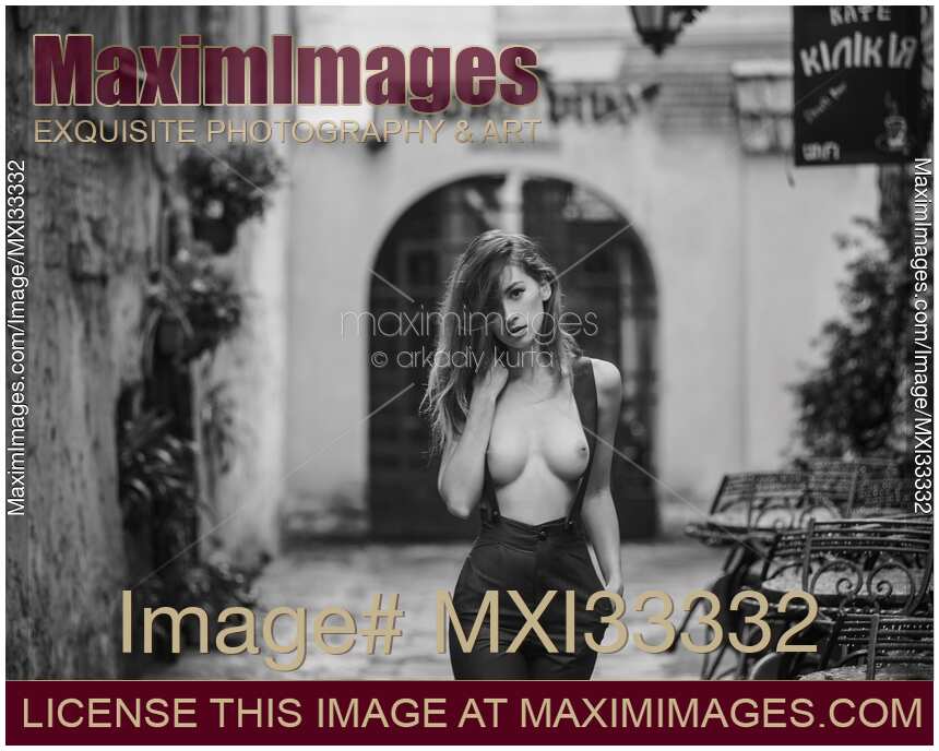 Woman walking topless on the street in suspender pants revealing her bare breasts Black and white