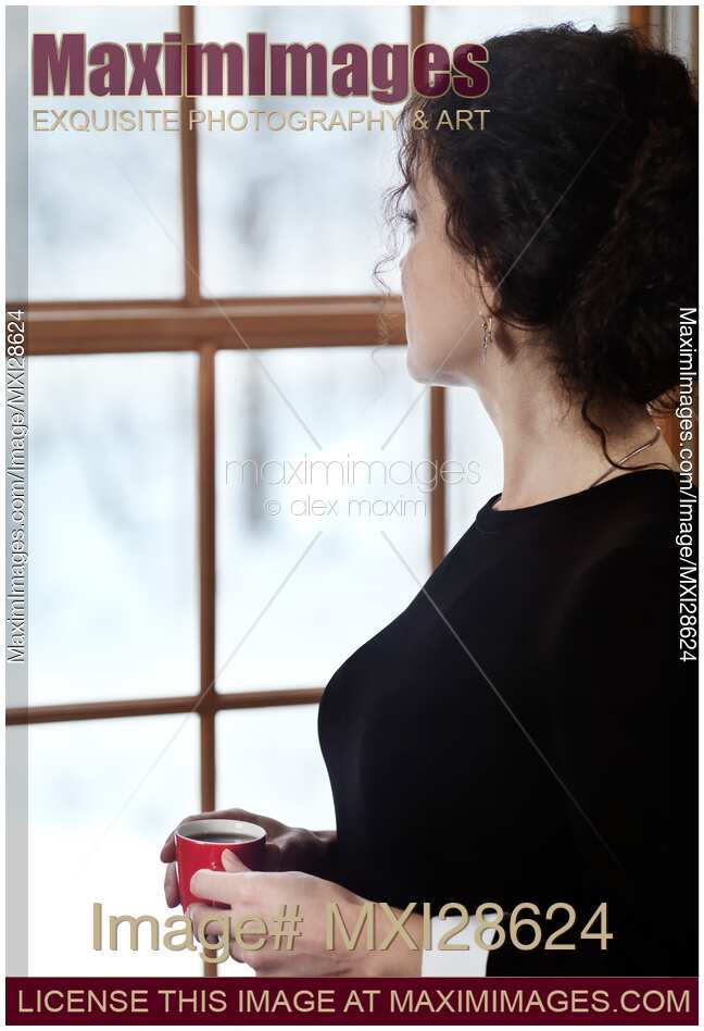 Woman with a cup of coffee standing by the window in winter