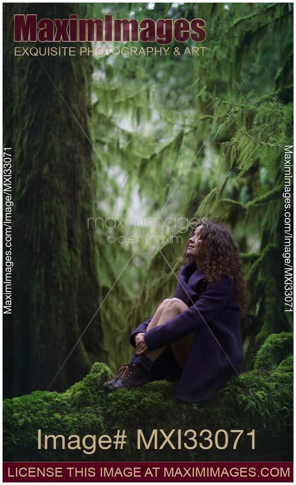 Woman with a dreamy expression sitting on a mossy tree trunk in ancient green forest moody nature scenery