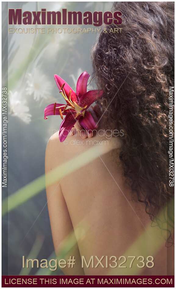 Woman with a lily flower on her shoulder her back with bare skin and long hair