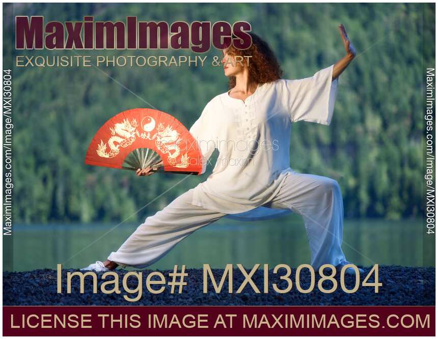 Woman with a red fan practicing Tai Chi Pu Bu stance at the lake shore in the nature