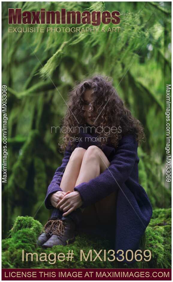 Woman with long curly hair and dreamy expression sitting in tranquil mossy green forest nature scenery
