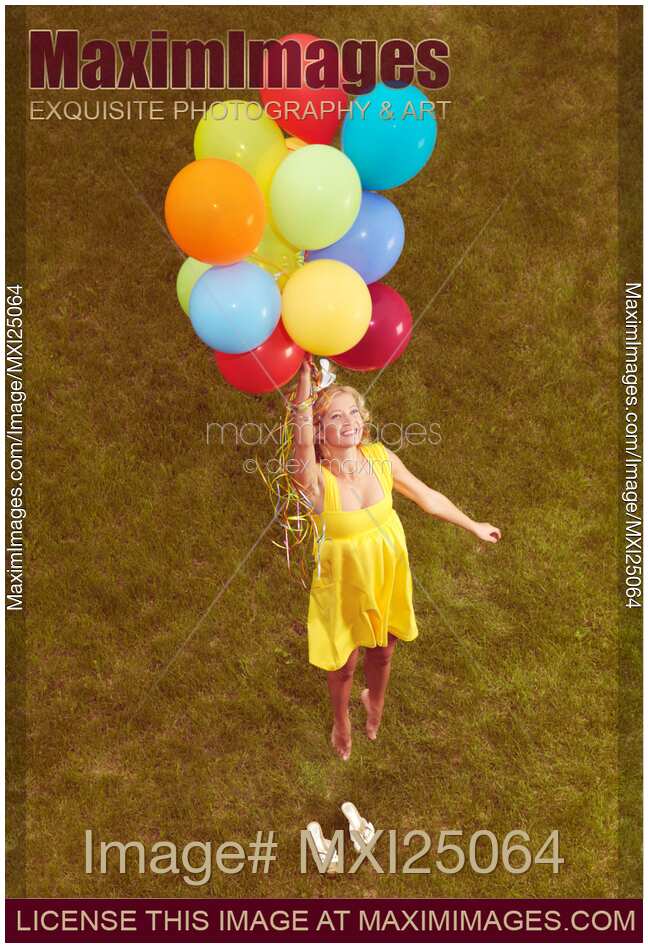 Young happy woman flying on colorful helium balloons