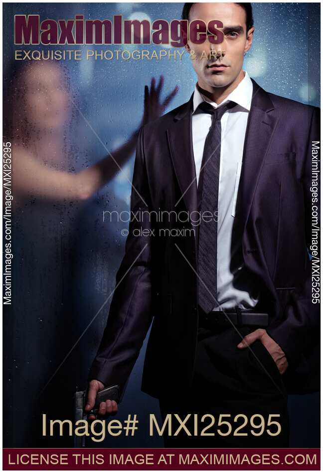 Young man in a suit with a gun in his hand and woman behind glass. Dramatic couple relationship portrait.