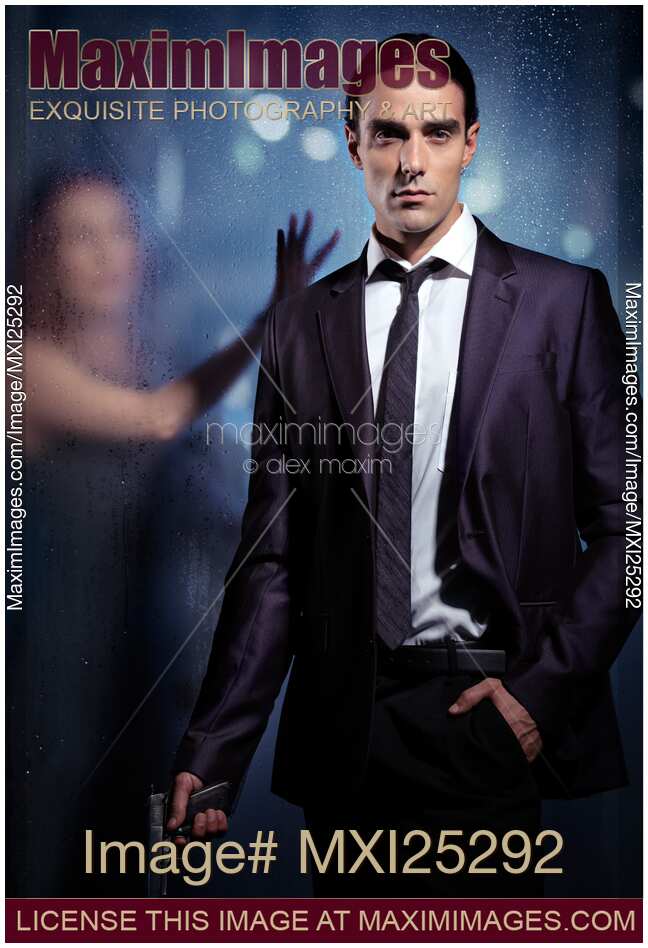 Young man in suit with a gun and woman behind glass