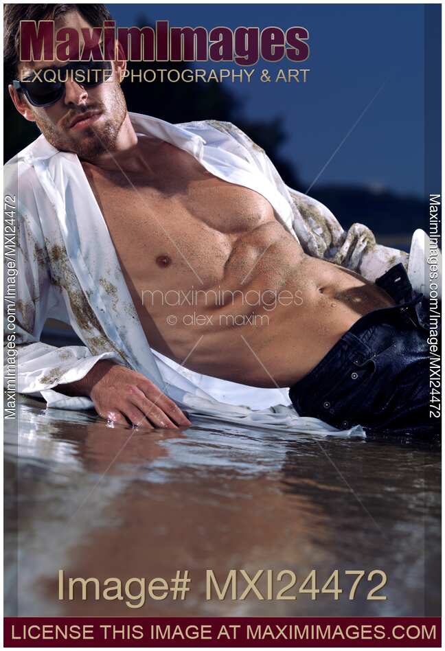 Young man lying on a sea shore in unbottoned wet shirt