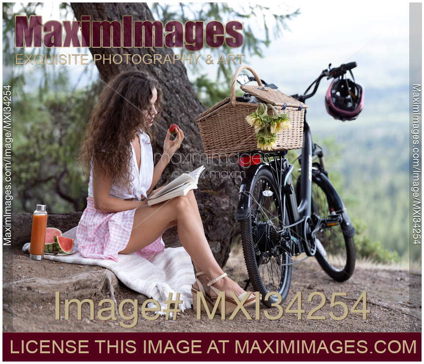Young pretty woman reading a book enjoying a little picnic in summer countryside with an e-bike by her side