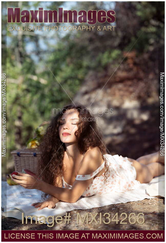 Young woman enjoying herself at a picnic in the nature with a book in sunshine