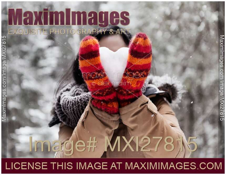 Young woman holding heart made of snow in her hands