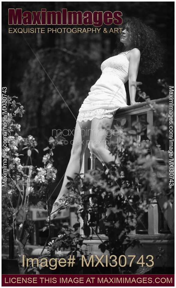 Young woman in a summer dress sitting on blacony railings in a garden enjoying sunshine